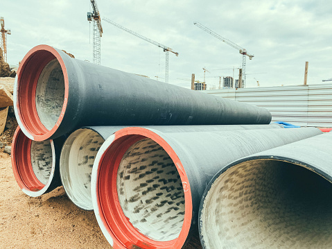 polypropylene pipes made of black material lie on a construction site. laying of sanitary communications. nearby cranes erect high concrete houses.