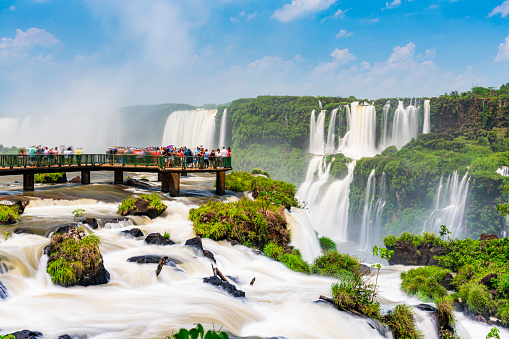 Tourists enjoying the falls on the footbridge into the water on a sunny day