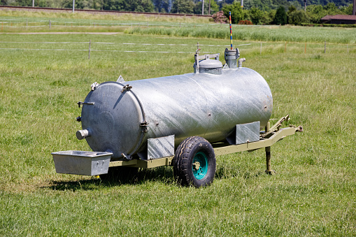 water trough metal aluminum for cows, these trailers are mobile and can be quickly parked in any place, green meadow, without animals and people, daytime, sunshine.