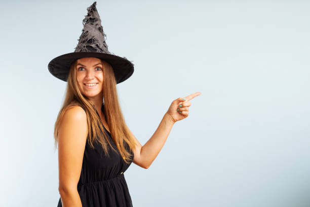istock Woman in witch costume pointing with finger at copyspace side and looking at camera on blue background. Happy Halloween 1420211200