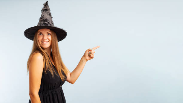 istock Woman in witch costume pointing with finger at copyspace side and looking at camera on blue background. Happy Halloween 1420211201