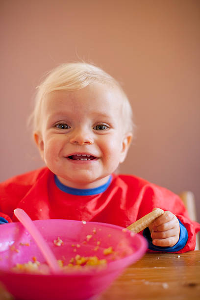 lächelnd baby mädchen essen am tisch - @jackstar stock-fotos und bilder