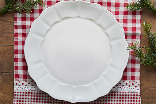 White empty holiday plate, on a decorated wooden table with Christmas tree branches
