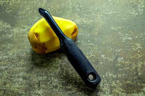 Top down view of a swivel metal vegetable peeler and potato