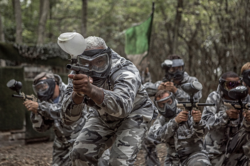 A mixed race middle aged male paintball team in action