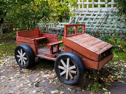 Wooden red handmade vintage car for children fun playing stand in a park at autumn day.