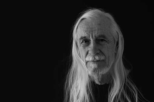 Low key studio  black and white portrait of smiling attractive old man with loose long gray hair. Horizontally.
