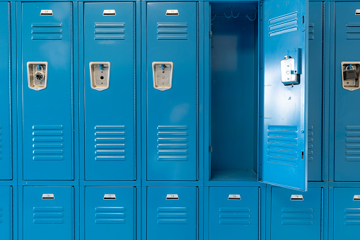 Un solo casillero de metal azul vacío abierto a lo largo de un pasillo anodino en una escuela secundaria típica de los Estados Unidos.  No se incluye información identificable y no hay nadie en el pasillo. photo