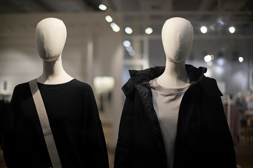 Two mannequins in black clothes. Fabric mannequin without facial features. Showcase of outerwear store. Details of shopping center.