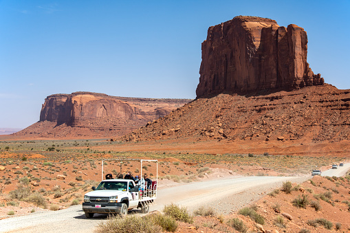 A group of tourists are on a tour of Monument Valley in a tour buggy on the scenic drive. Camel Butte is visible in the background. \nMonument Valley, AZ, USA\n05/20/2022