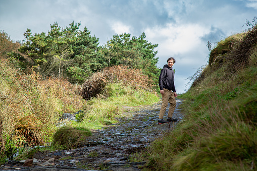 Caucasian man hiker standing on a trail looking back. Nohoval Cove, County Cork, Ireland