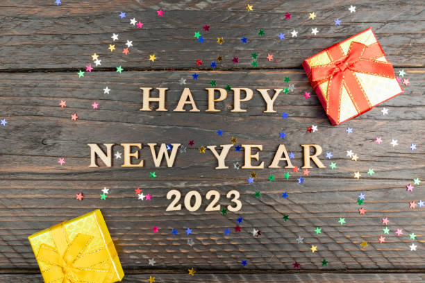 istock Happy new year 2023 next and red and yellow small gift boxes on dark wooden background with confetti. 1420249058