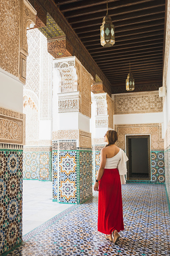 young latin woman dressed in a red skirt and a soft blouse, admiring the beauty of the architecture of a Moroccan palace, looking for her inner peace.