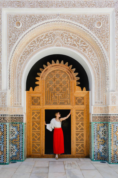 young latin woman dressed in a red skirt and a soft blouse, posing in the wooden frame of an ancient Moroccan palace.