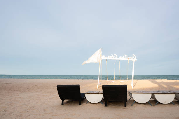 istock White sand beach with white chairs and swings, blue sky background. 1420272143
