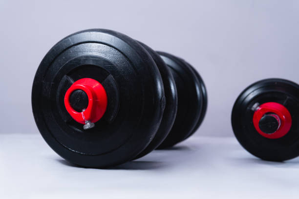 istock Black dumbbells on a white background. Gym weights on a table. Large dumbbell and small dumbbell for training in the gym 1420291521