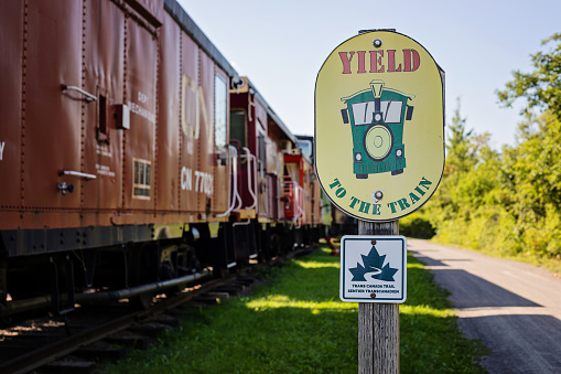 Tatamagouche, Canada - August 21, 2022. A sign alongside the Trans-Canada Trail alerts travelers to yield to the train; an old train sits beside the sign.
