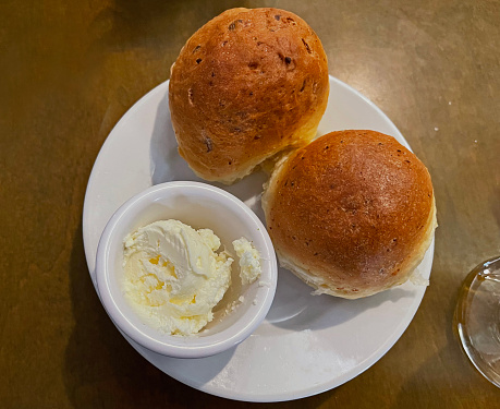 Two dinner rolls on a white bread plate.   White, ceramic ramekin of butter on the plate.