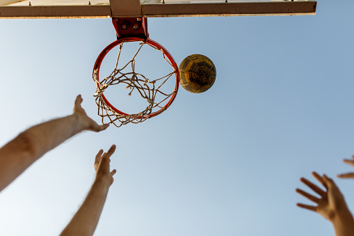 Directly below shot of hands of unrecognizable father and teenage son throwing a basket ball in the hoop while playing on outdoors court.