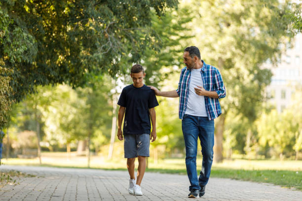 Sad teenage boy going for a walk with his father who is consoling him stock photo