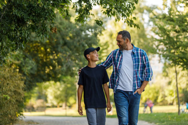 Front view of father and son walking embraced at the park, chatting and bonding stock photo