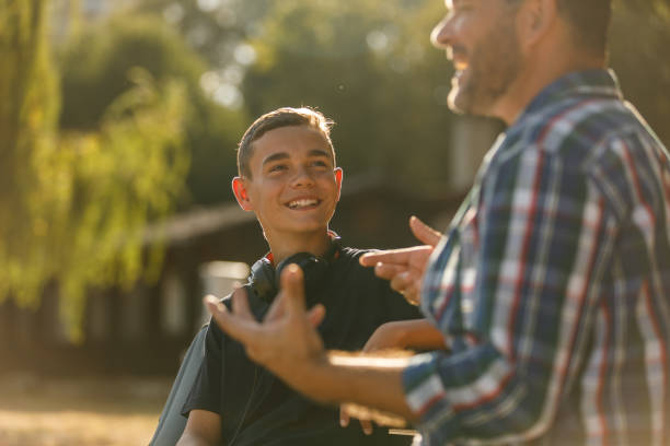 Man gesturing while sharing an interesting story with his teenage son stock photo