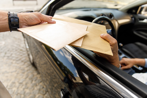Close up shot of unrecognizable delivery man giving envelopes to a customer in a car at the curbside pickup.