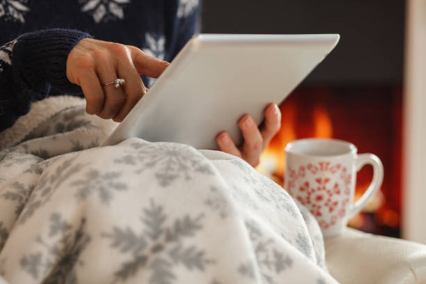 istock Woman scrolling on digital tablet while relaxing under a cozy blanket and enjoying coffee 1420305199