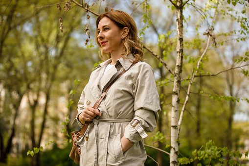 Low angle view of smiling mid adult woman going for a relaxing walk at the public park when going home from work.