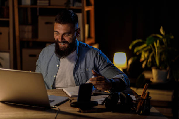 istock Cheerful young man video chatting with a business partner while working late 1420306550