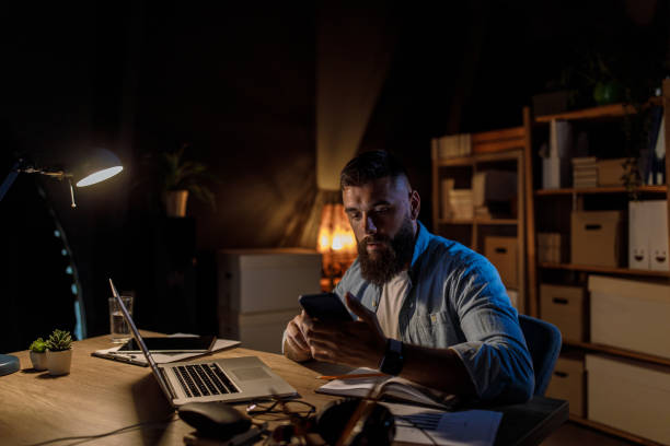 istock Young man working late at his desk, checking text messages via smart phone 1420306551