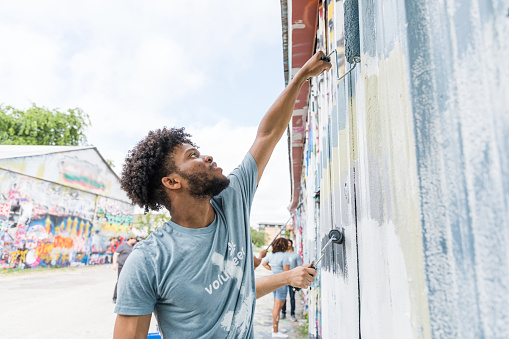 The young adult male helps to work on the mural painting on the side of the church building.