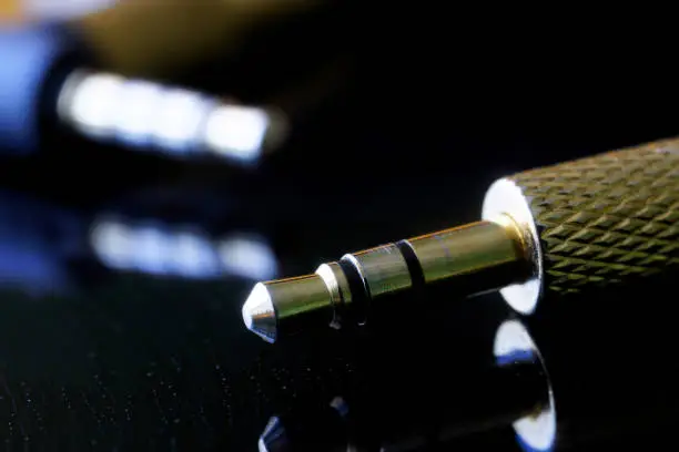 Gold-plated TRS connector for audio transmission on a wet black background. The concept of audiophile equipment. Mini-jack - 3.5 mm. Shallow depth of field. Selective focus. Macro.