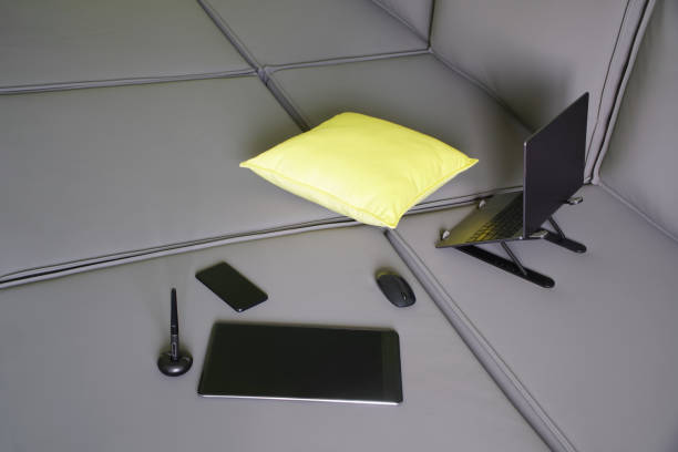 istock Silver thin laptop on stand, mobile phone, yellow pillow and graphics tablet with stylus on gray modular sofa. Concept of a comfortable remote work of a designer. Rest during work 1420308548
