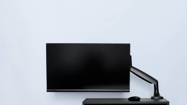 istock Modern thin computer monitor or TV set is mounted on a metal swivel desktop bracket with a gas lift function. Small black table. Off-center side holder. Copyspace 1420308601
