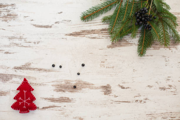 Directly above shot of Christmas tree branch with black berried and a red Christmas tree shaped ornament against a distressed wooden white background.