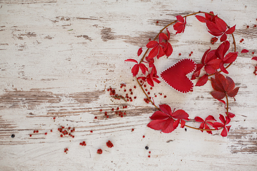 Directly above shot of a branch with red leaves shaped like a heart around a heart shaped Christmas ornament against a distressed white background with copy space.