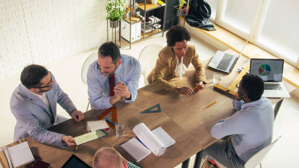 istock Group of architects sitting at conference table, chatting about projects in motion 1420310942