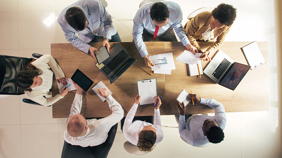 Directly above shot of diverse group of corporate business people sitting around conference table, having a project meeting.