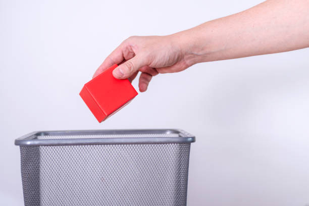 istock Man tosses gift box into trash can against gray background. 1420311874