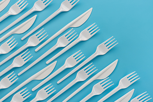 Pattern, template, background, studio shot. Ornorazovye white plastic knives and forks on a blue background. The concept of ecology and recycling of plastic waste.