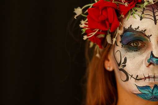 Cut out shot of beautiful mid adult woman, in sugar skull face paint, looking at camera.