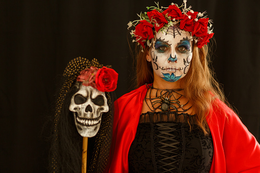 Copy space shot of beautiful mid adult woman wearing a Halloween costume and a sugar skull make up while holding a staff with a gipsy skull. She is looking at camera with a slight smile