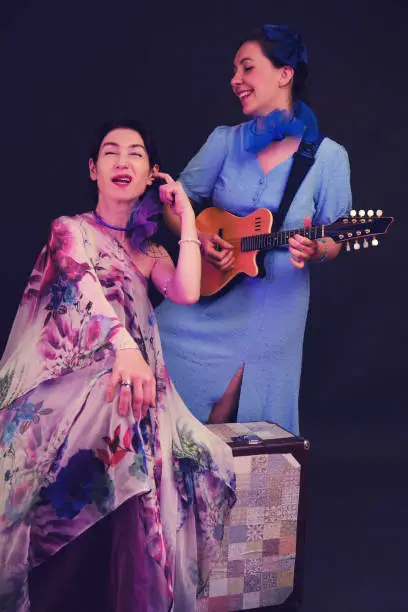 Photo of Women musicians in blue dresses with musical instruments on a black studio background. Happy artists with stringed musical instruments on a dark background