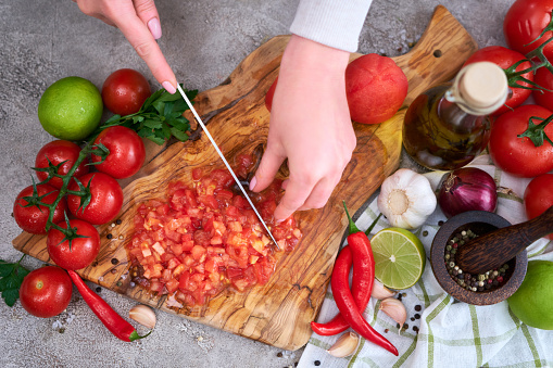 woman cutting and chopping blanched tomato by knife on wooden board.