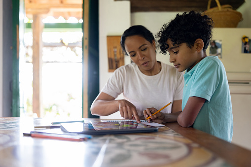 Latin American boy homeschooling with the assistance of his mother - education concepts