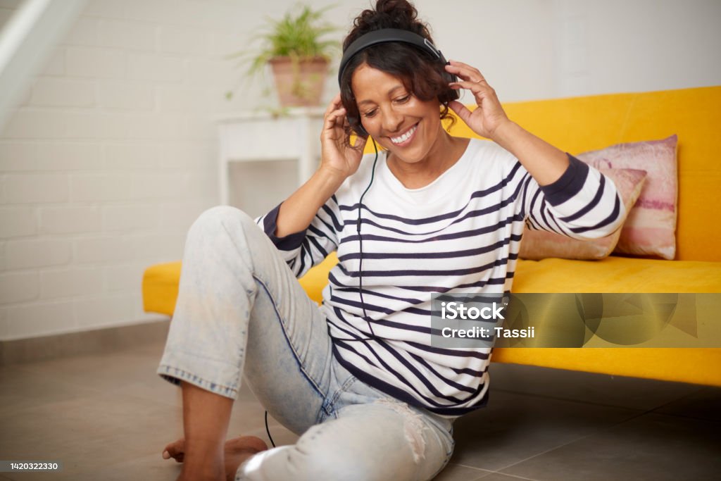 Music, relax and retirement with a senior or elderly woman listening with headphones on the floor at home. Carefree time to listen to the radio or audio while resting and relaxing in the living room Music Streaming Service Stock Photo