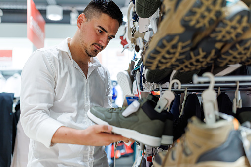 A young Caucasian man is taking a look at a pair of shoes while doing his seasonal shopping.
