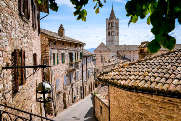 A beautiful stone alley in the medieval heart of Assisi in Umbria with the Basilica of Santa Chiara in background A glimpse of a beautiful alley in the historic center of the medieval town of Assisi, in Umbria. In the background the beautiful bell tower of the Basilica di Santa Chiara (St Claire Basilica). An ancient Umbrian city built starting from the 9th century BC, Assisi became in 89 BC an important center of social and economic domination of Ancient Rome. After the fall of Rome and countless looting due to the barbarian invasions, in the Middle Ages Assisi was conquered by the Byzantines and the Lombards, finally ending up under the dominion of the emperor Frederick I the Barbarossa. Assisi is world famous for being the city of San Francesco and Santa Chiara (St Francis and St Claire), recognized as a place of spirituality and peace between all peoples and different confessions. The Umbria region, considered the green lung of Italy for its wooded mountains, is characterized by a perfect integration between nature and the presence of man, in a context of environmental sustainability and healthy life. In addition to its immense artistic and historical heritage, Umbria is famous for its food and wine production and for the quality of the olive oil produced in these lands. Since 2000 the Basilica and other Franciscan sites of Assisi have been declared a World Heritage Site by UNESCO. Image in high definition format. basilica di santa chiara assisi stock pictures, royalty-free photos & images