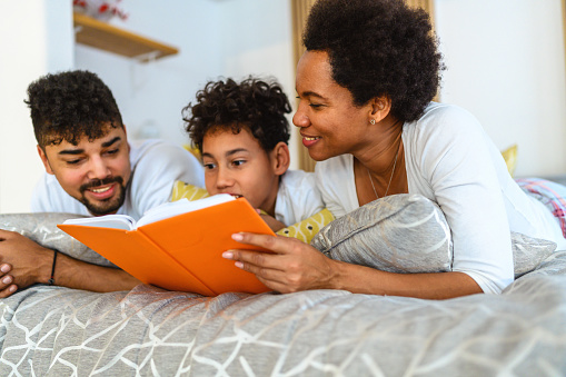 Shot of a black family reading a book in bed at home